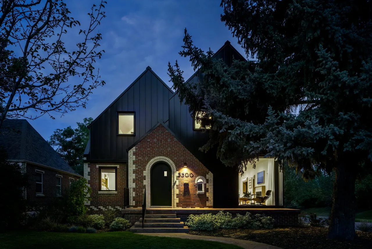 Night view of a brick and dark metal-clad house with gable roof and illuminated interior windows.