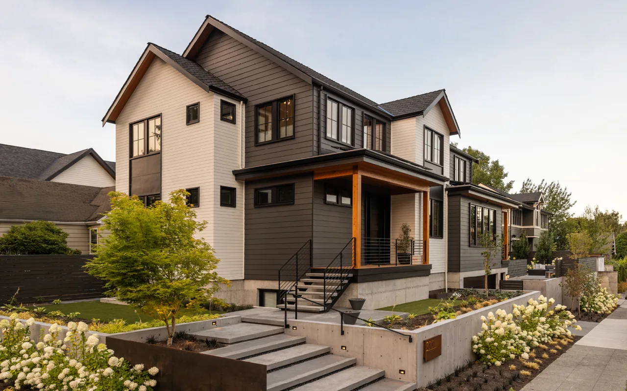 Exterior front view of a two-story transitional style house with dark and white siding, concrete steps, and a covered porch with wood posts.