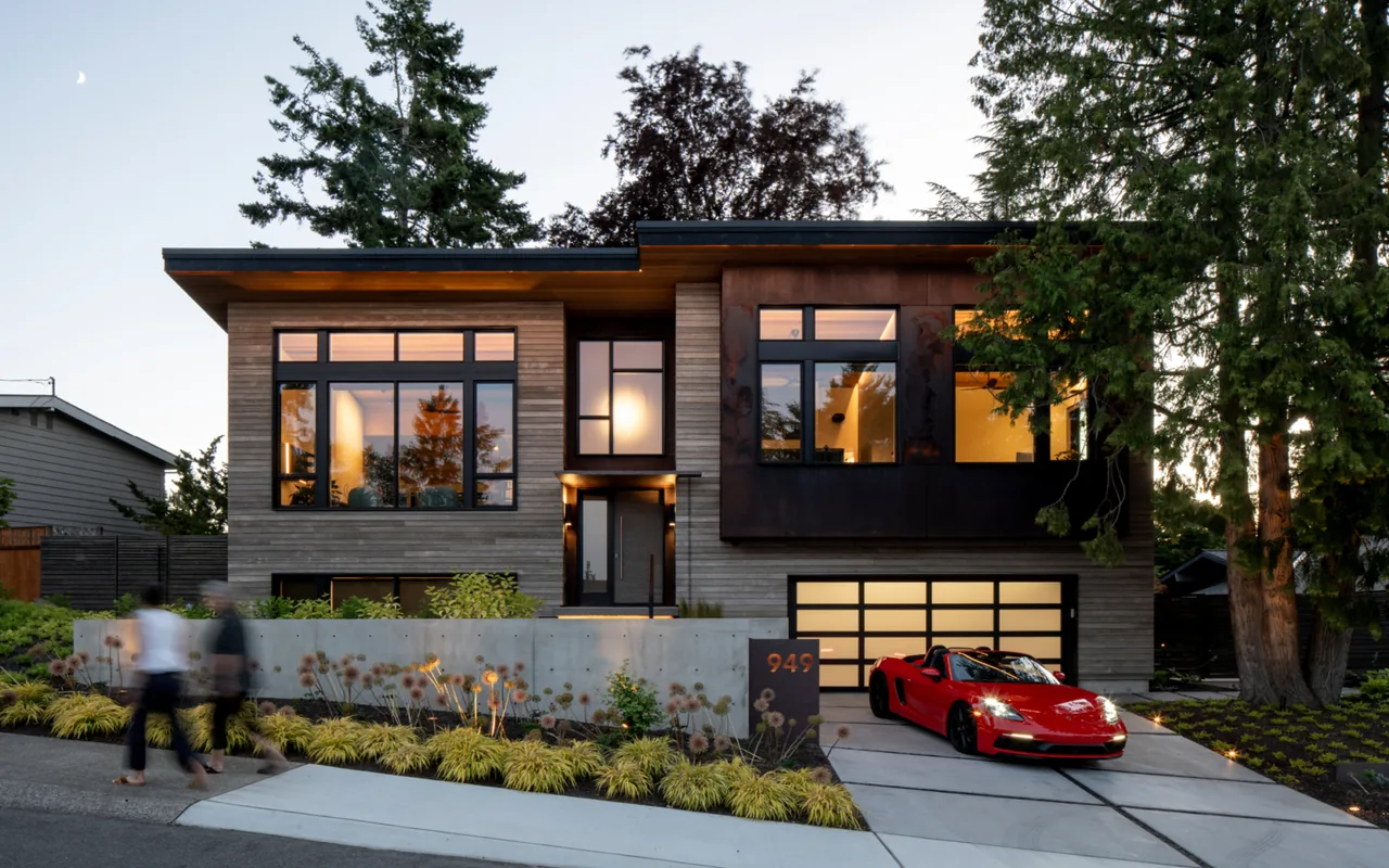 Modern split-level house exterior at dusk with horizontal wood siding and large black-framed windows.