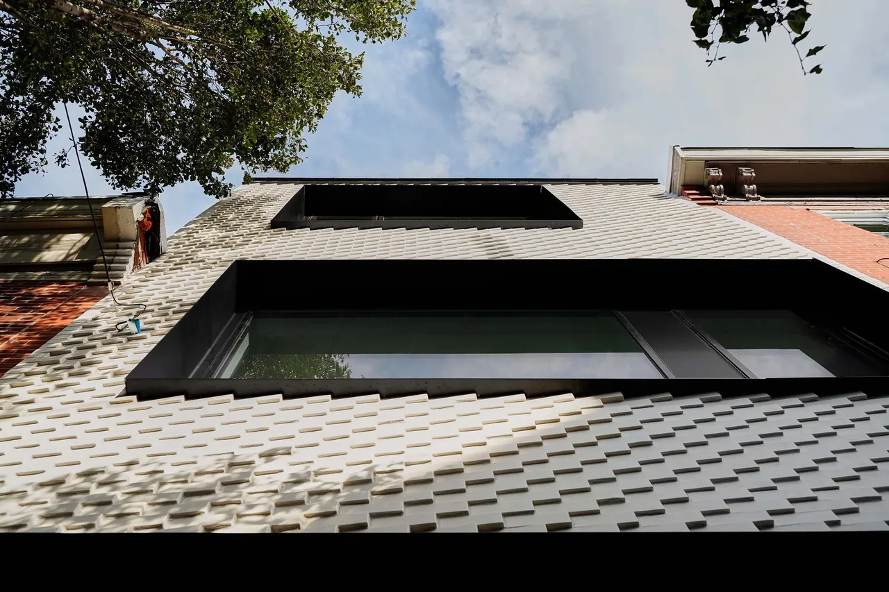 Upward view of a modern exterior wall with white textured bricks and two horizontal black-framed windows.