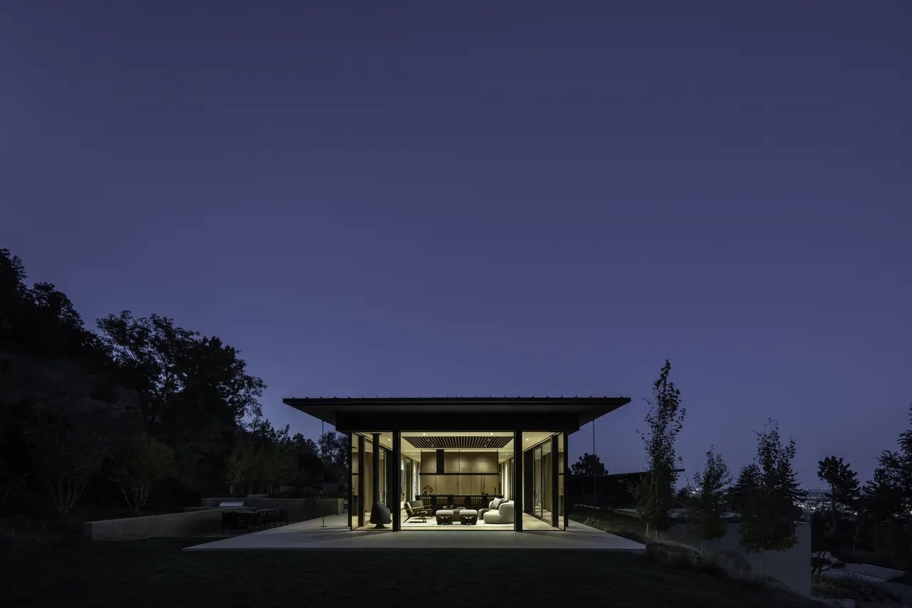 Night view of a modern house with an illuminated interior and large glass walls under a flat roof.