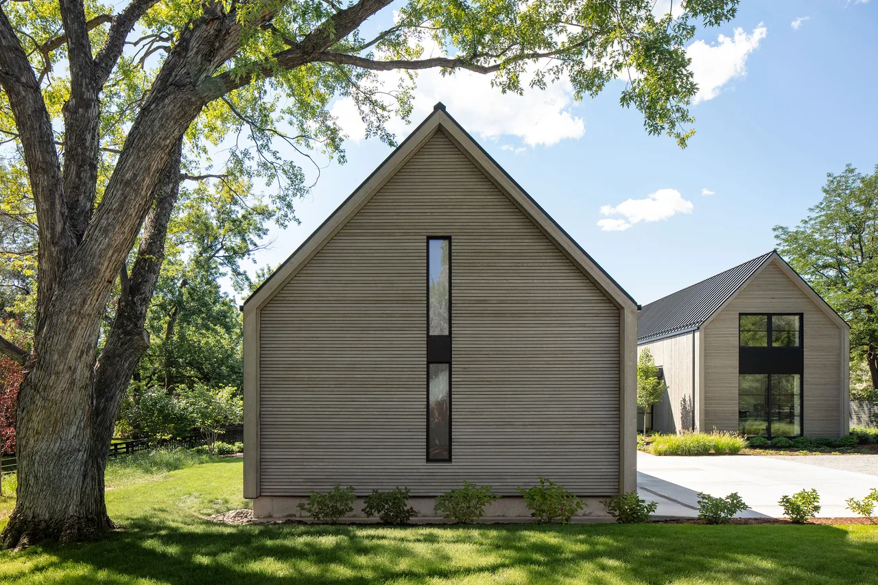 Exterior view of two modern gable-roofed buildings clad in wood siding surrounded by green grass and trees.