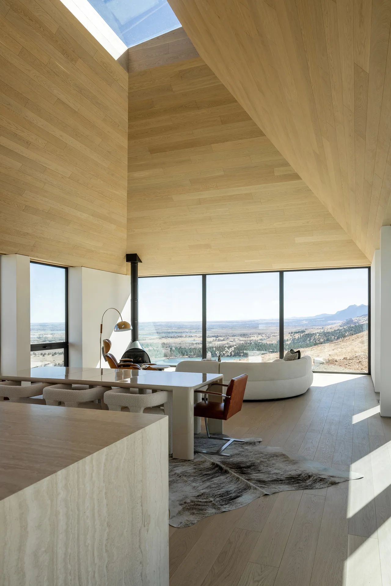 Interior living space with large windows overlooking a vast natural landscape and a wood-paneled vaulted ceiling with a skylight.