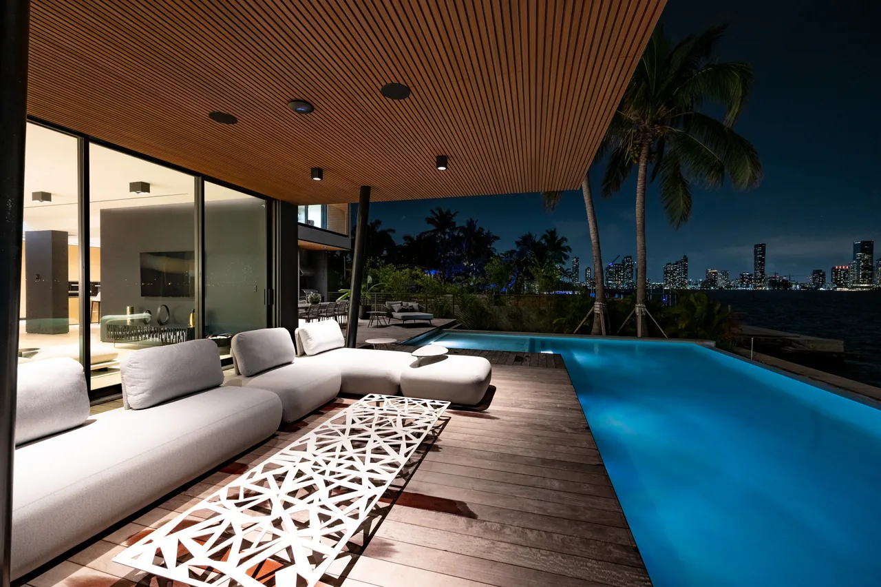 Outdoor patio at night with modular white cushioned seating and an illuminated pool overlooking a city skyline and palm trees.