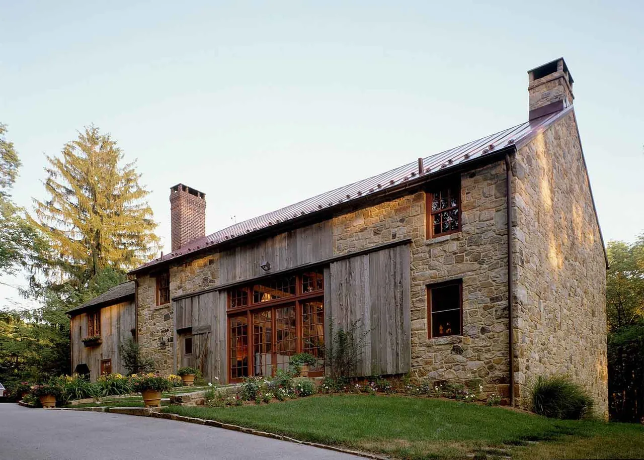 Stone and wood barn-style house with large windows and a metal roof under clear sky.