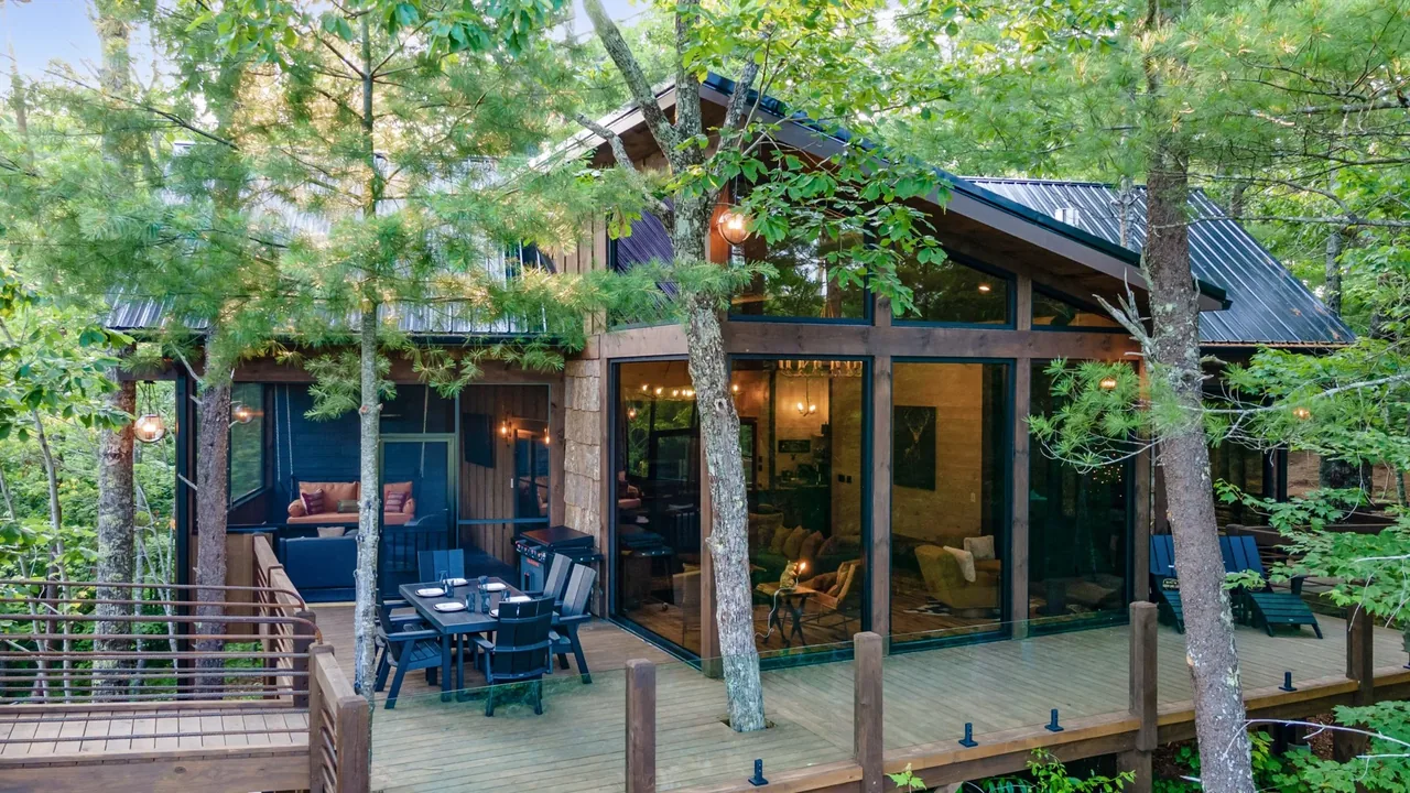 A modern wood cabin with large floor-to-ceiling windows and a spacious deck integrated with surrounding trees.