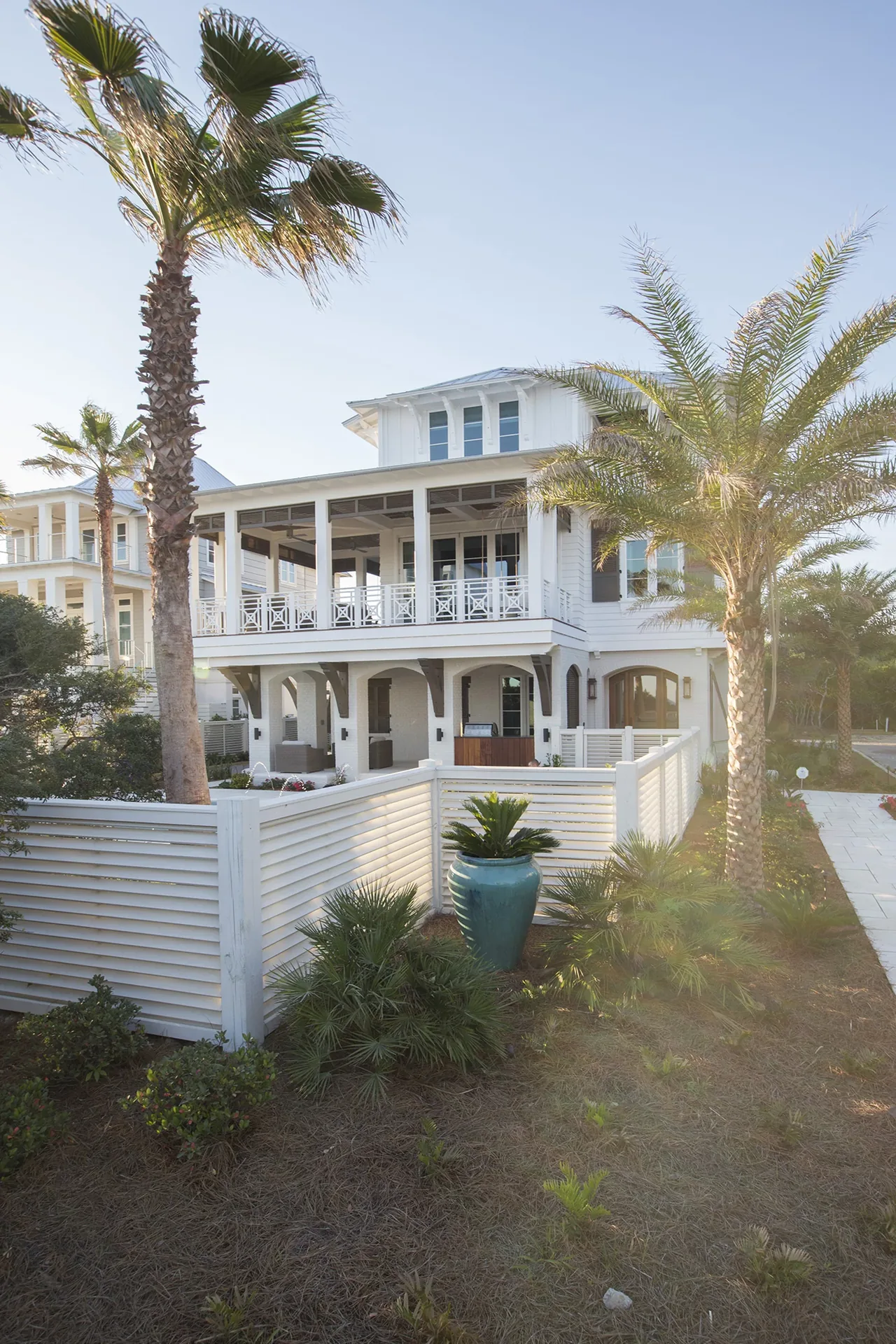 Exterior of a two-story white beach house with a covered porch and palm trees in the yard.