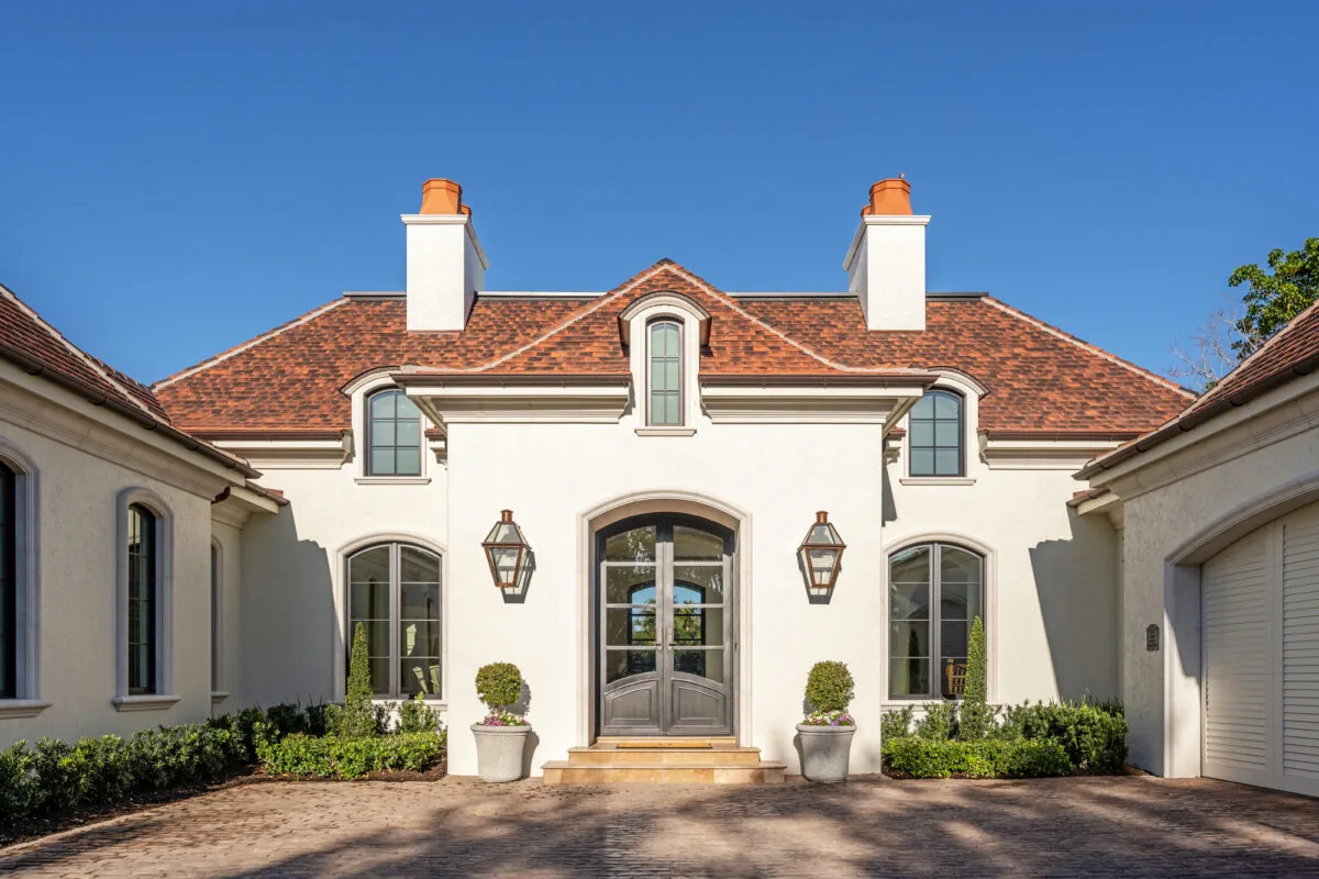 Front exterior of a French countryside style house with a stucco facade, arched windows, and a detailed red tile roof.