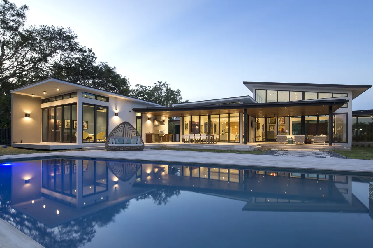 Twilight view of a modern home with large windows and an outdoor pool reflecting the building and trees.
