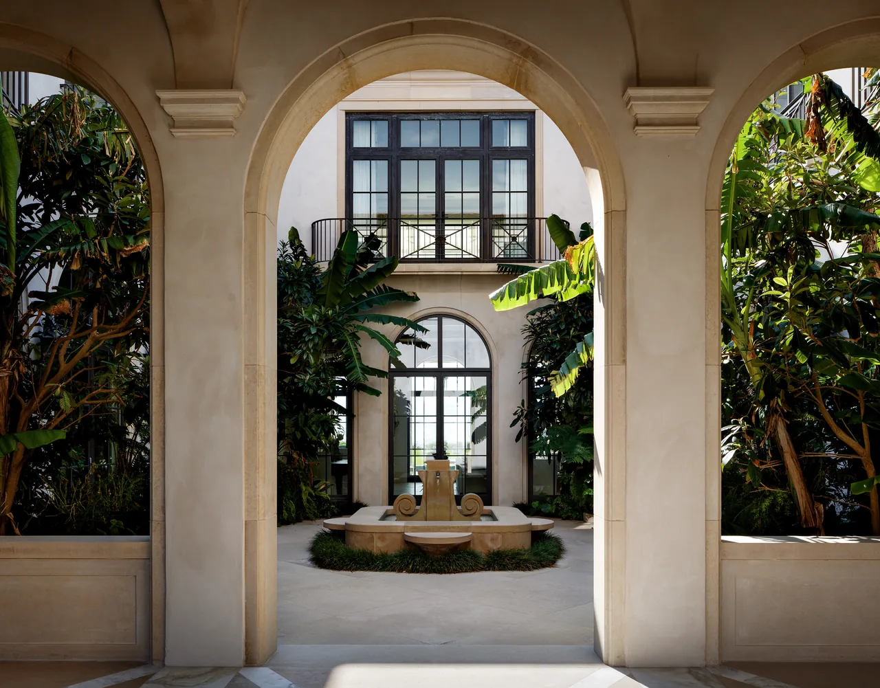 View through a stucco arched courtyard with a central stone fountain and lush greenery.