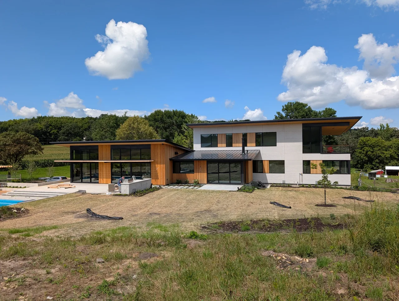 Modern two-story house with wood and light siding, wide overhangs, large windows, and a landscaped yard on a sunny day.