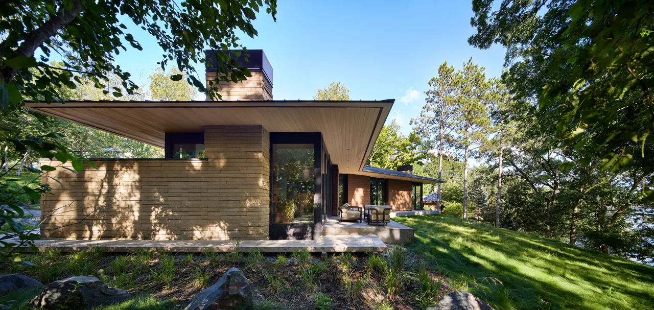 Modern one-story house with extended flat roof and brick exterior surrounded by trees and greenery.