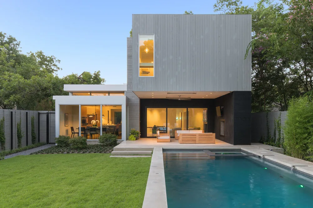 Modern two-story house with a backyard pool and outdoor seating area illuminated at dusk.