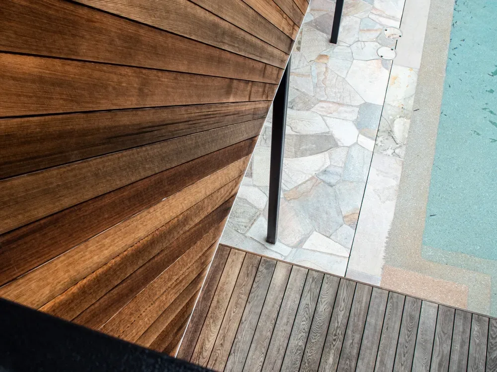 Outdoor area showing a wood siding wall, wood deck floor, stone patio, and edge of a swimming pool.
