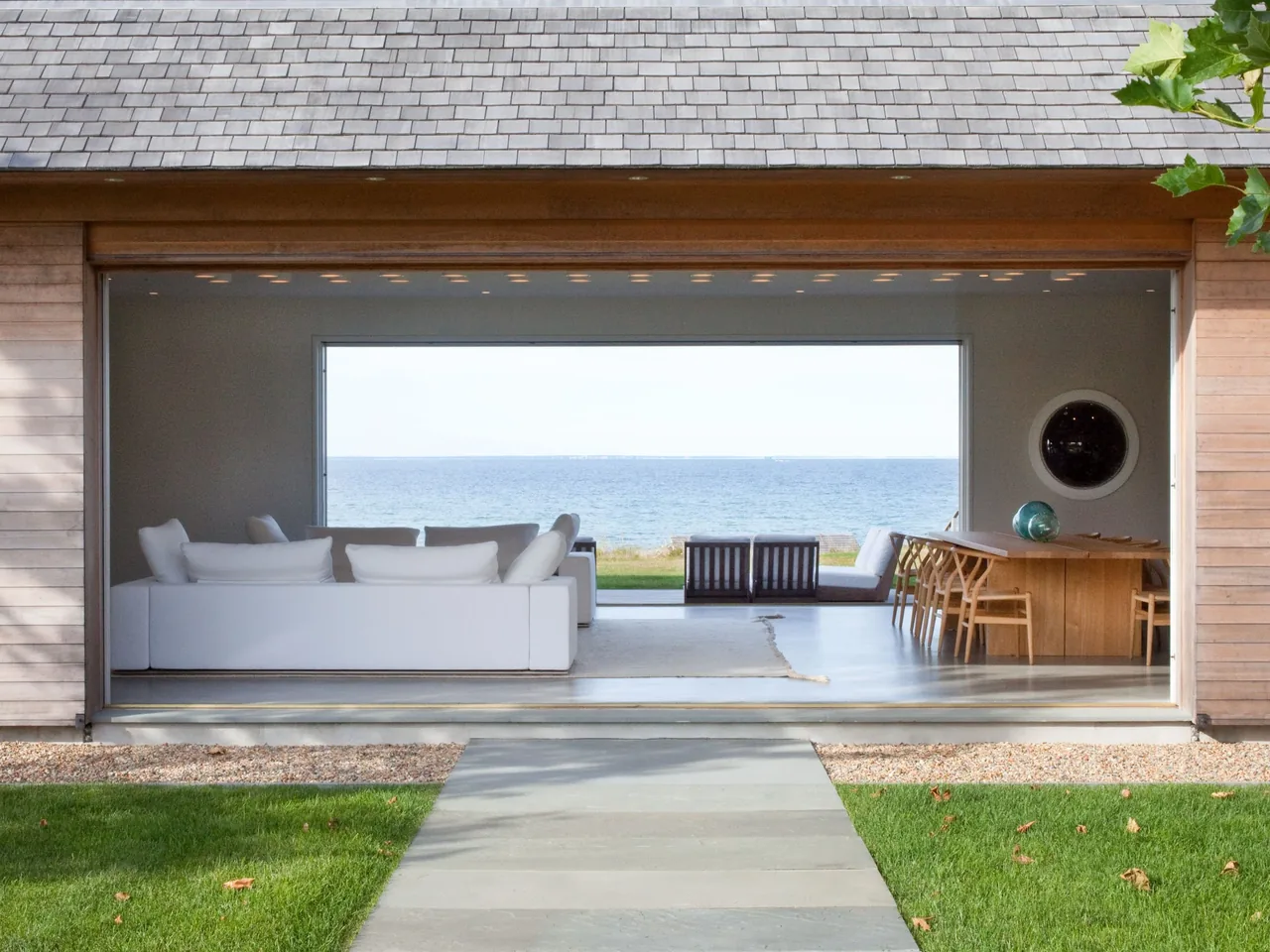 Open living and dining area of a modern house with a large picture window overlooking the ocean.