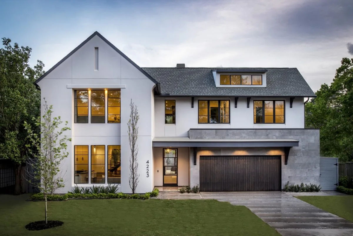 Front exterior view of a two-story modern house with white walls, black window frames, and a double garage door at dusk.