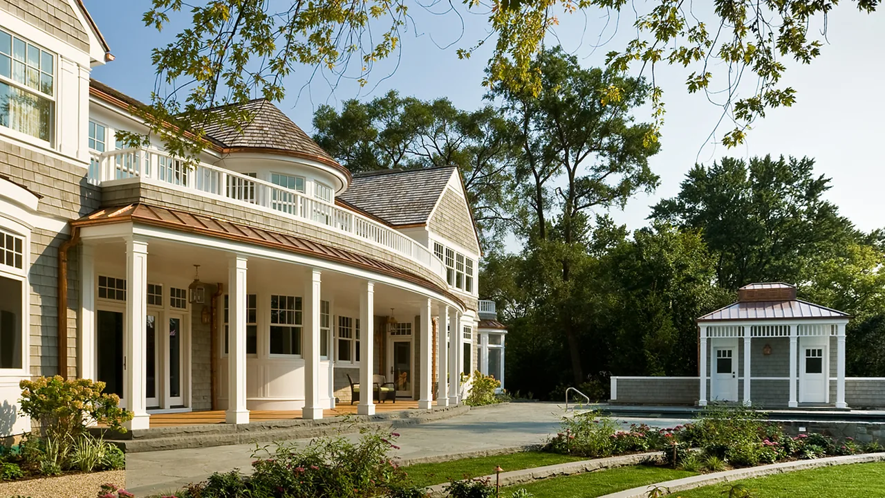 Large curved porch of a house with stone steps and a poolside gateway structure in a landscaped yard.