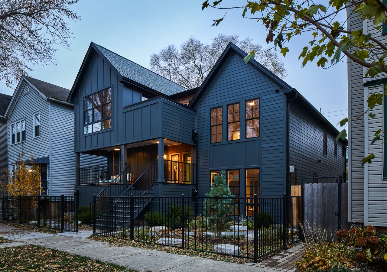 A modern dark blue two-story house with gable roofs and large windows at dusk.