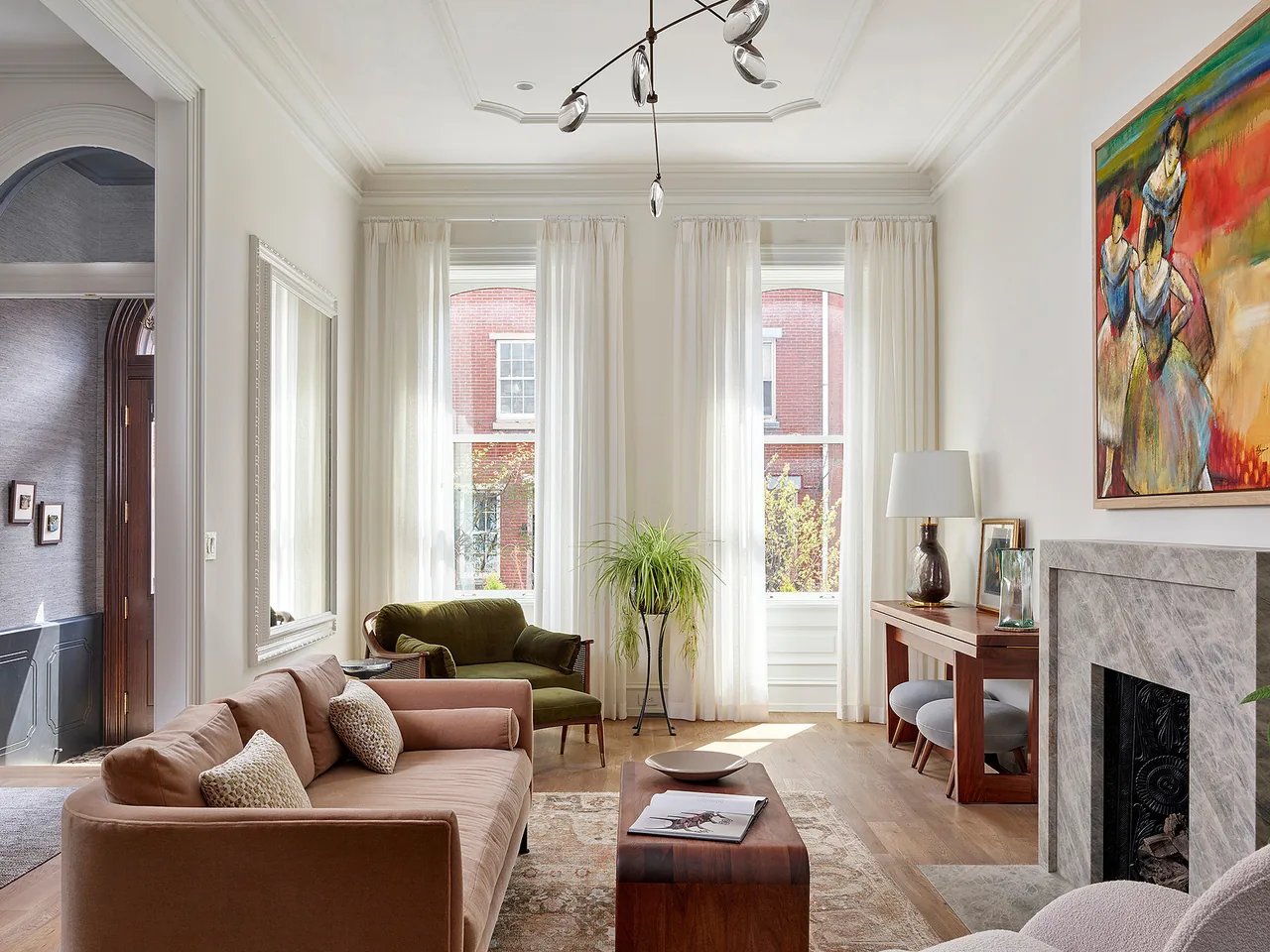 Living room with tall windows, beige and green seating, a wood coffee table, and a gray stone fireplace.