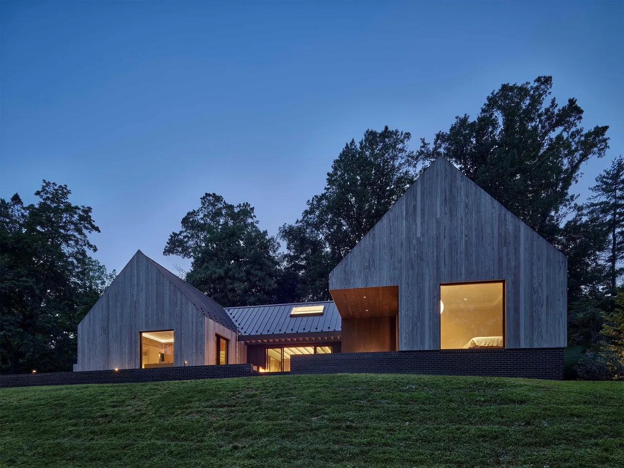 Exterior view of a modern residence at dusk with wood siding and large windows.