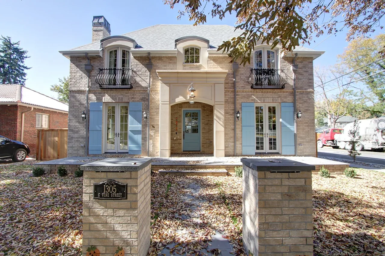 Front view of a two-story brick house with blue shutters and a central blue door under a light-colored stone archway.