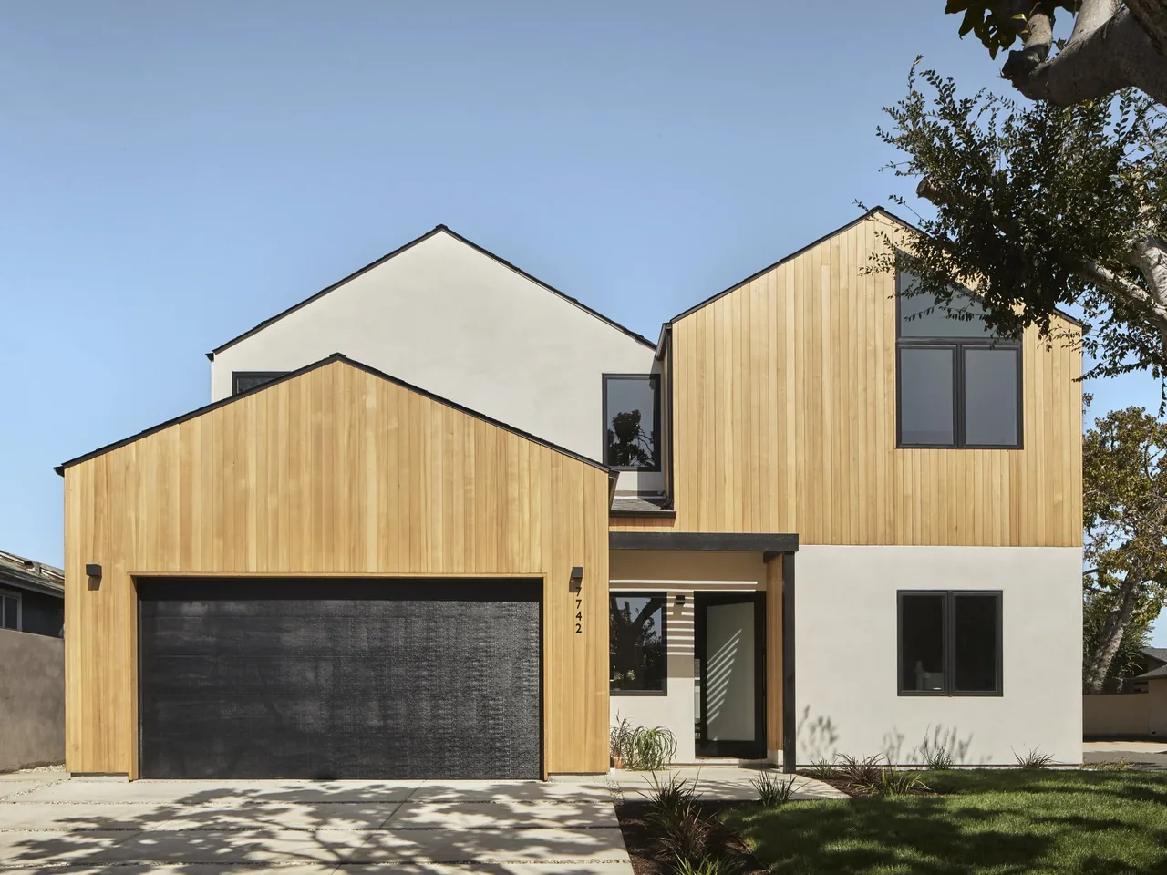 Two-story residence with a mix of wood siding and white stucco exterior and black framed windows and doors.