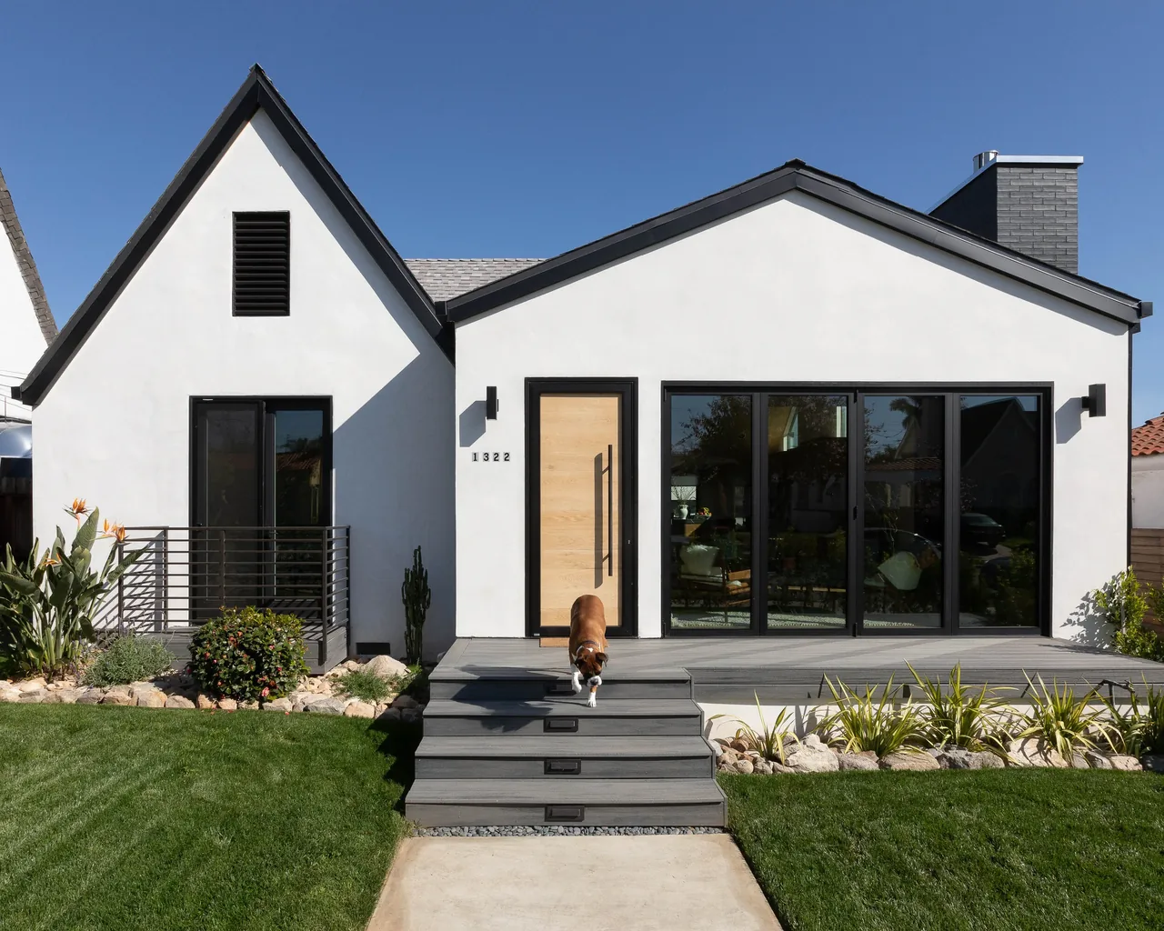Front exterior of a white residential house with black window frames, a light wood door, and a gray deck with steps and landscaping.