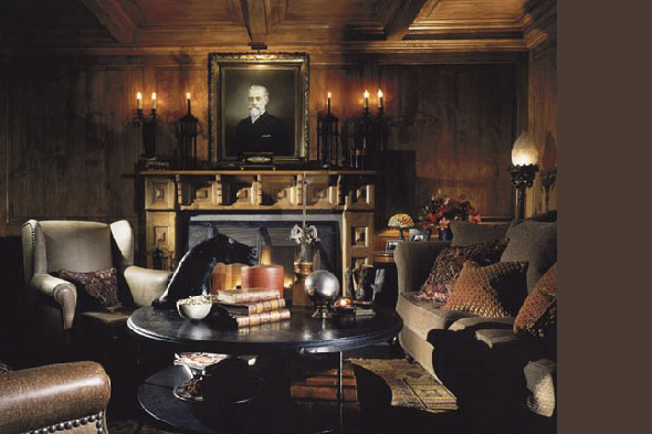 A richly decorated living room with dark wood paneling, a fireplace, and a black coffee table with decorative objects.
