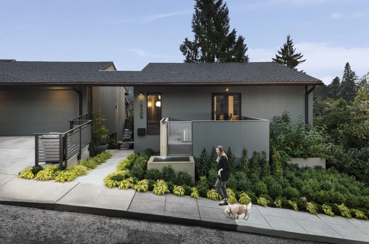 Exterior front view of a single-story gray house with a sloped roof and landscaped garden in front.