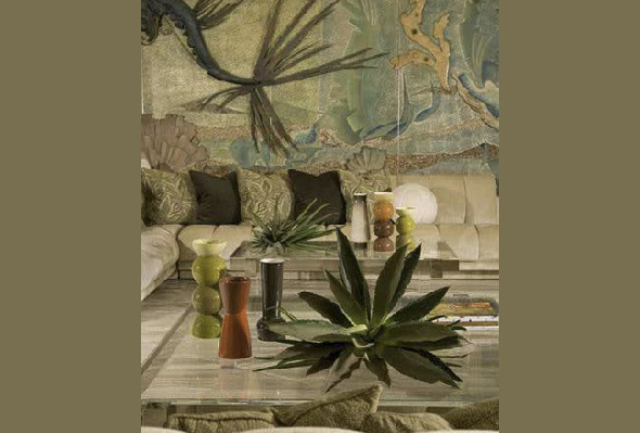 Living room with beige sectional sofa and a coffee table decorated with plants and accessories, set against an artistic textured wall.