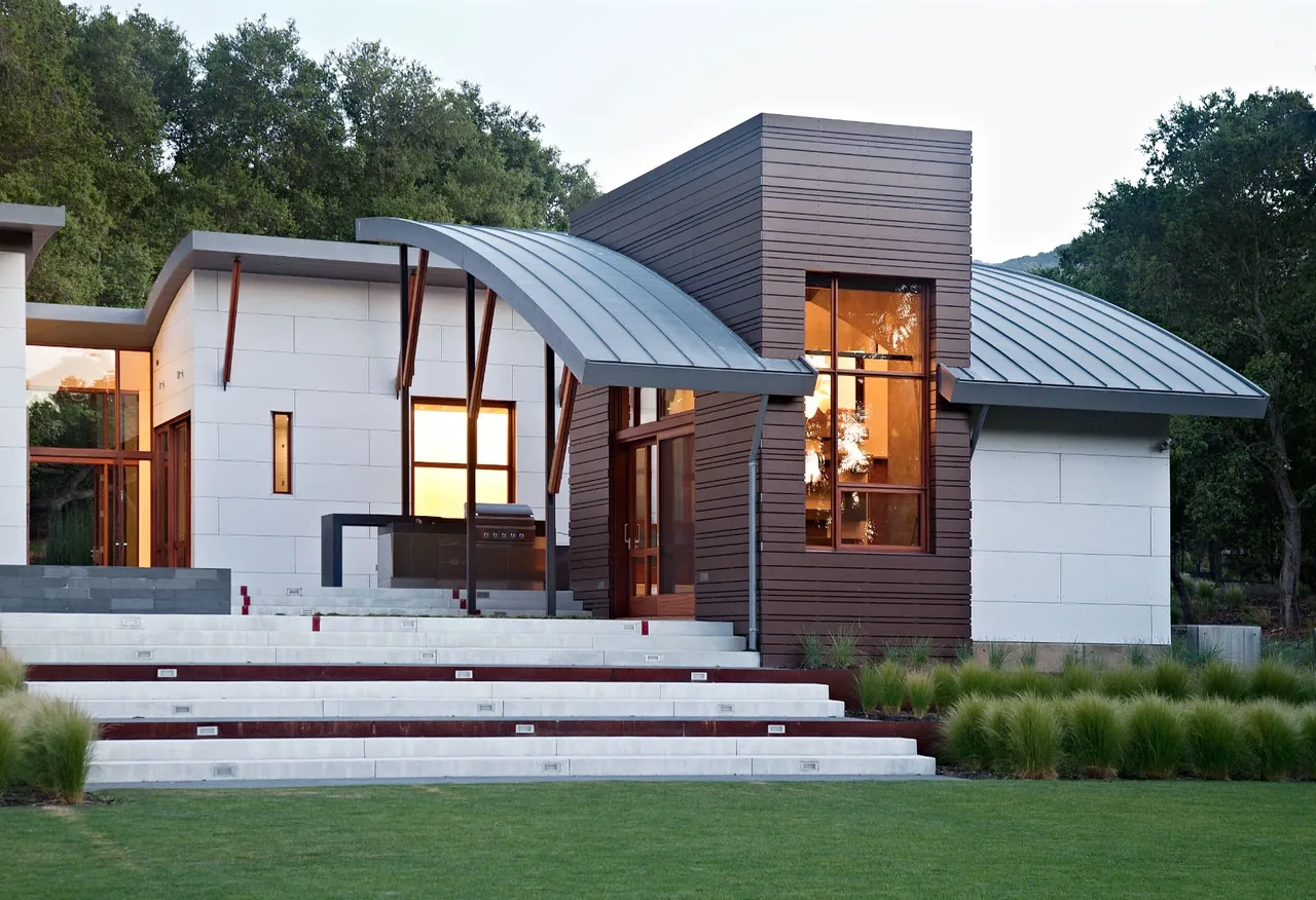 Exterior view of a modern house featuring a curved metal roof and a mix of wood siding and white panel walls.