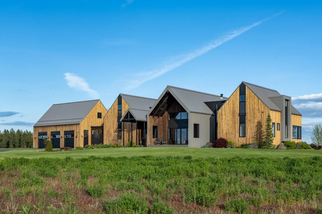 Exterior view of a large modern farmhouse with multiple gable roofs and wood siding under a clear blue sky.