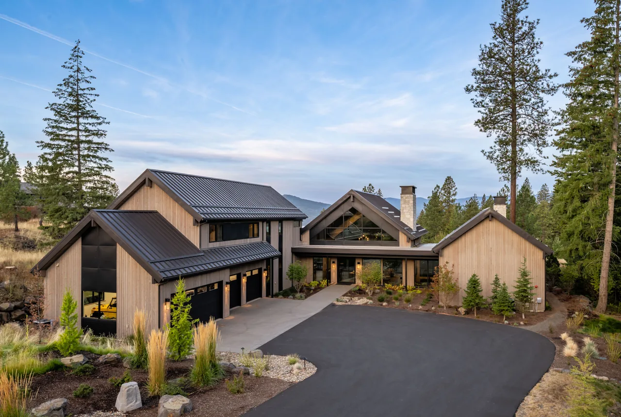 Exterior front view of a modern house with light wood siding and black metal roof in a wooded landscape.