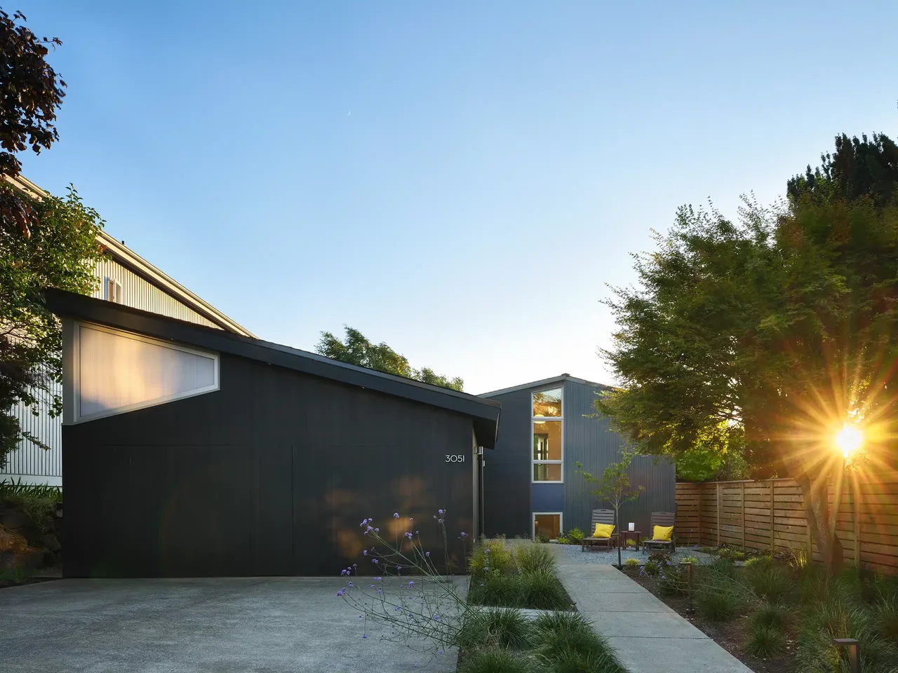 Exterior view of a mid-century modern home with black siding and a sloped roof at sunset.