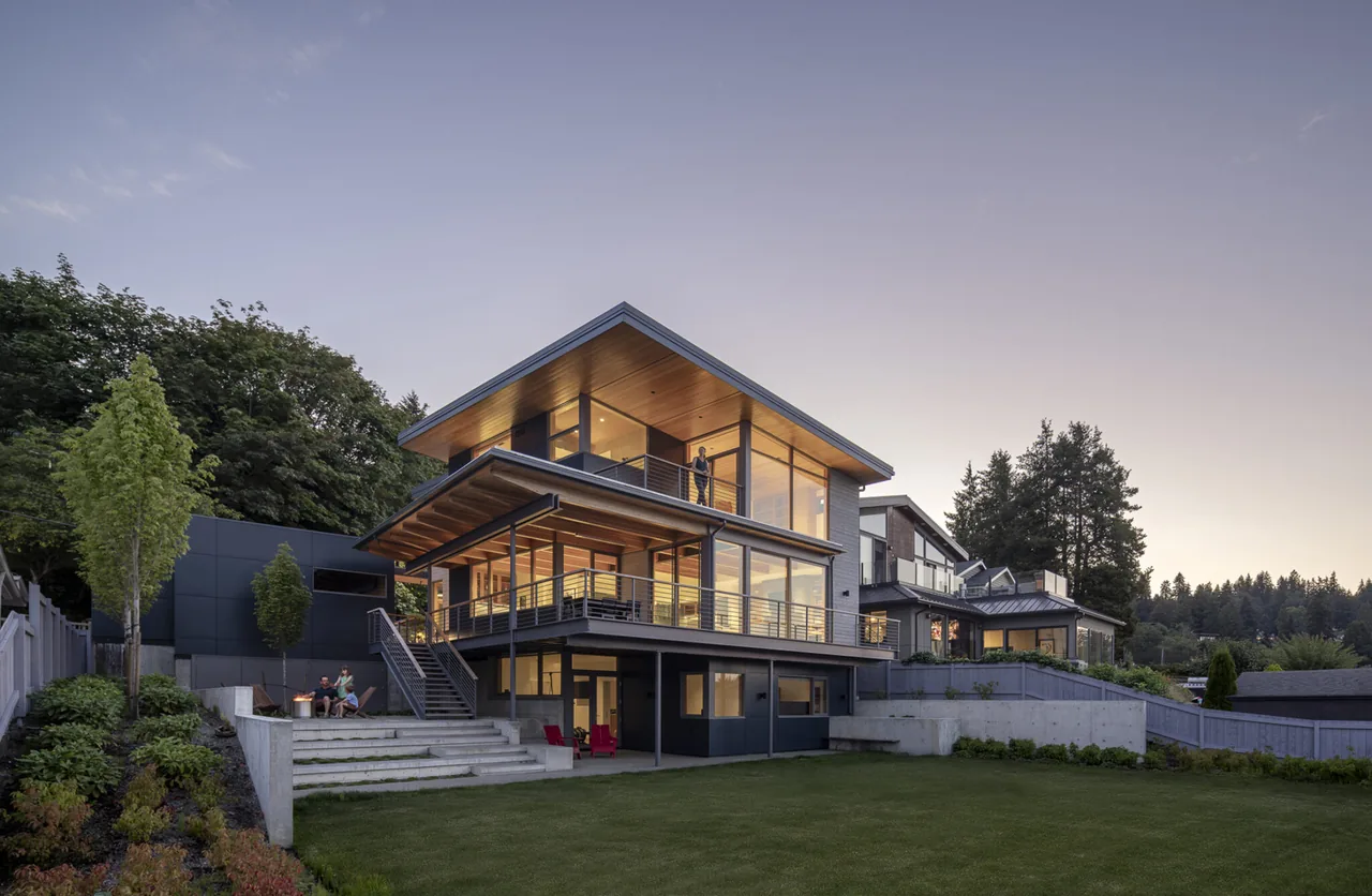 Modern multi-level home with large windows and extended rooflines in a landscaped yard at dusk.