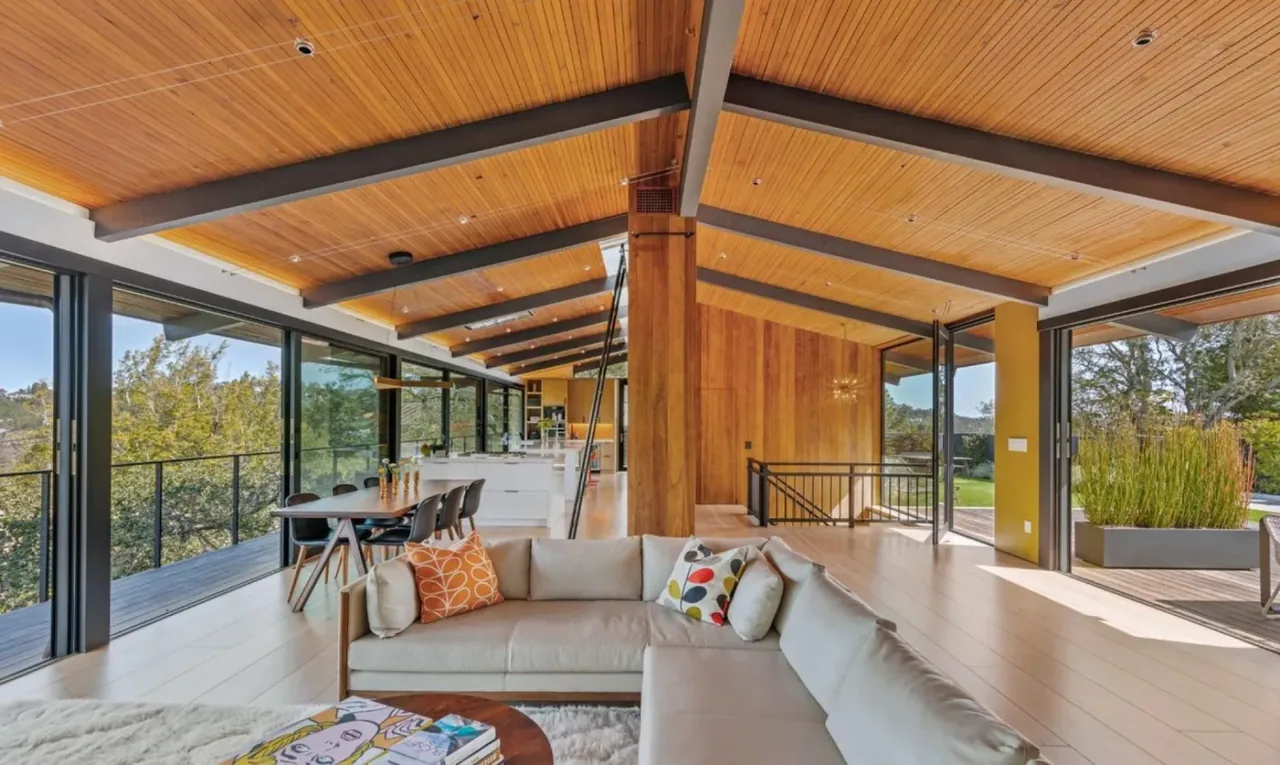 Interior of a mid-century modern living and dining area with wooden ceiling and large glass windows.
