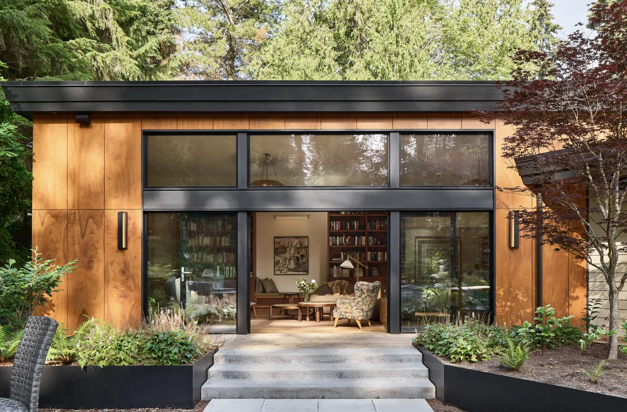 Exterior view of a modern house with wood siding, large black-framed windows, and lush landscaping.
