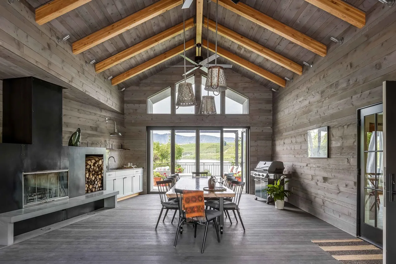 Interior dining area with vaulted ceiling, wooden beams, and large glass doors opening to a lakeside deck.