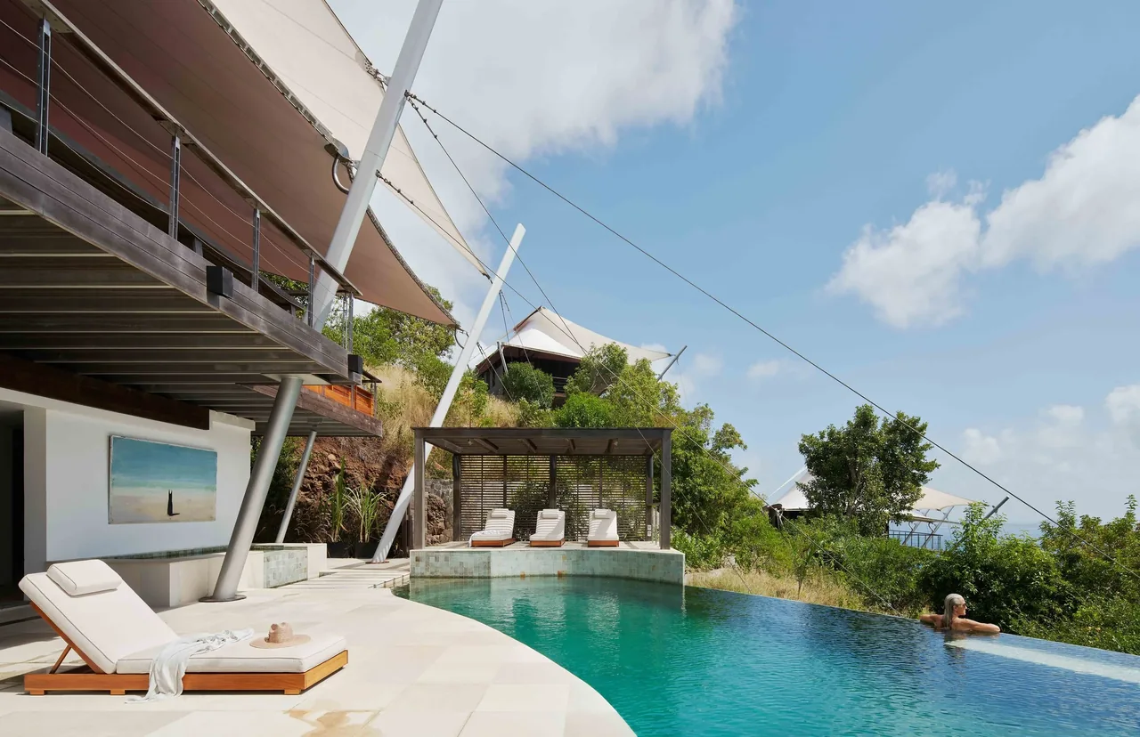 Outdoor infinity pool with lounge chairs and fabric shade sails on a sunny day.