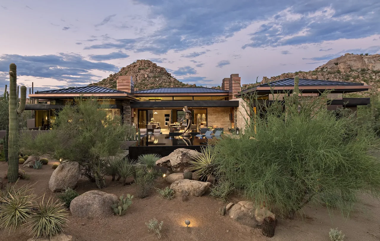 Front view of the Silversmith Residence in desert landscape with rocky hills at dusk.