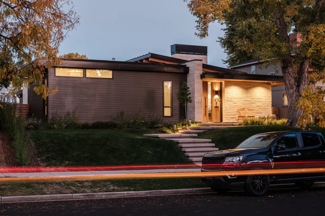Exterior view of a modern single-story house at dusk with horizontal siding and stone walls, illuminated entrance, and a black pickup truck.