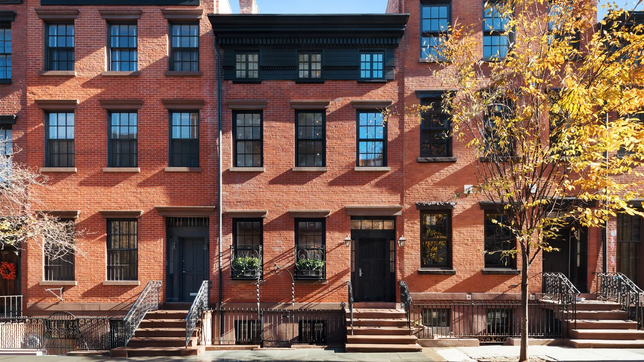 Red brick townhouse with black window frames and stairs leading to the main entrance on a sunny day with trees.