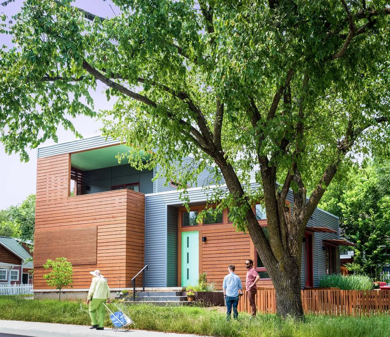 Modern two-story house with a mix of wood siding and horizontal metal siding framed by a large green tree in the front yard.