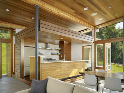 Interior view of a modern cabin kitchen and dining area with wood ceiling and large windows.